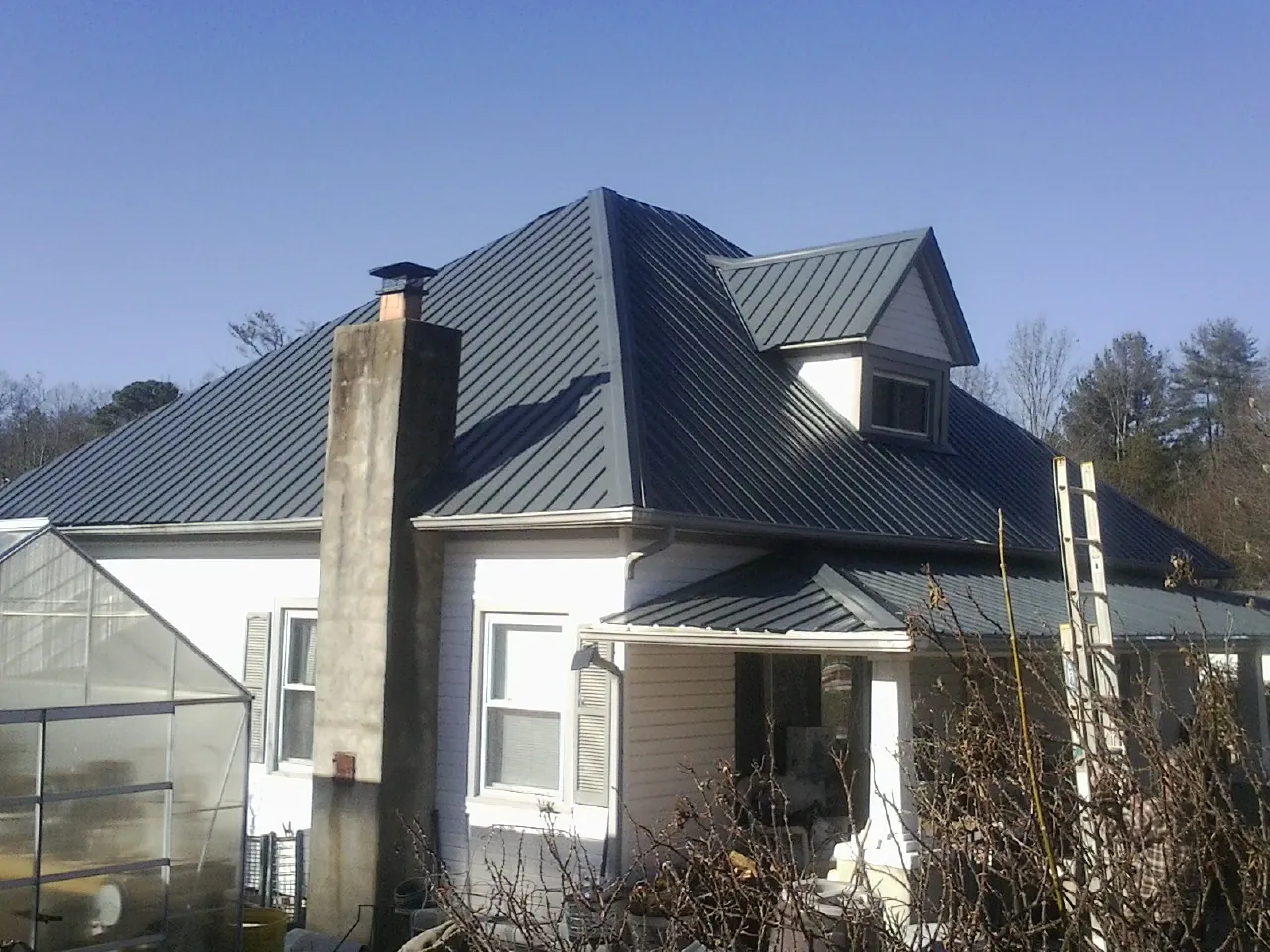 Dark blue standing seam metal roof on a white farmhouse with dormer — Slate & Tile Roof Repair by Roofing Brothers in Crum Lynne