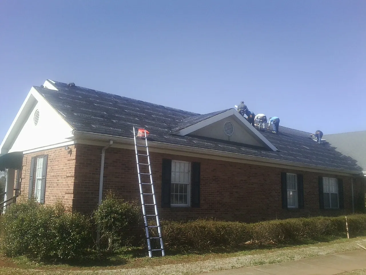 Crew tearing shingles off a brick ranch roof with a ladder set — Emergency Roof Repair work by our crew in Crum Lynne