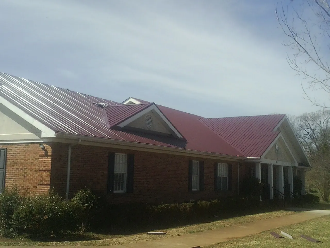 Red metal roof with gabled entries on a long brick building, from a Hail Damage Roof Repair job in Crum Lynne