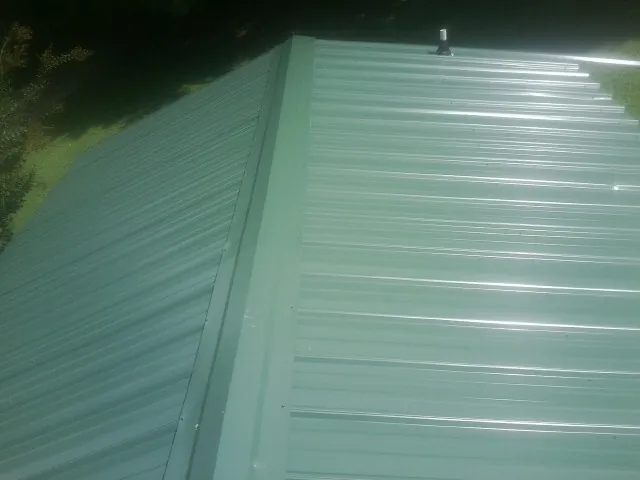 New green metal panels meeting at the ridge of a roof — Flat Roof Repair work by our crew in Crum Lynne