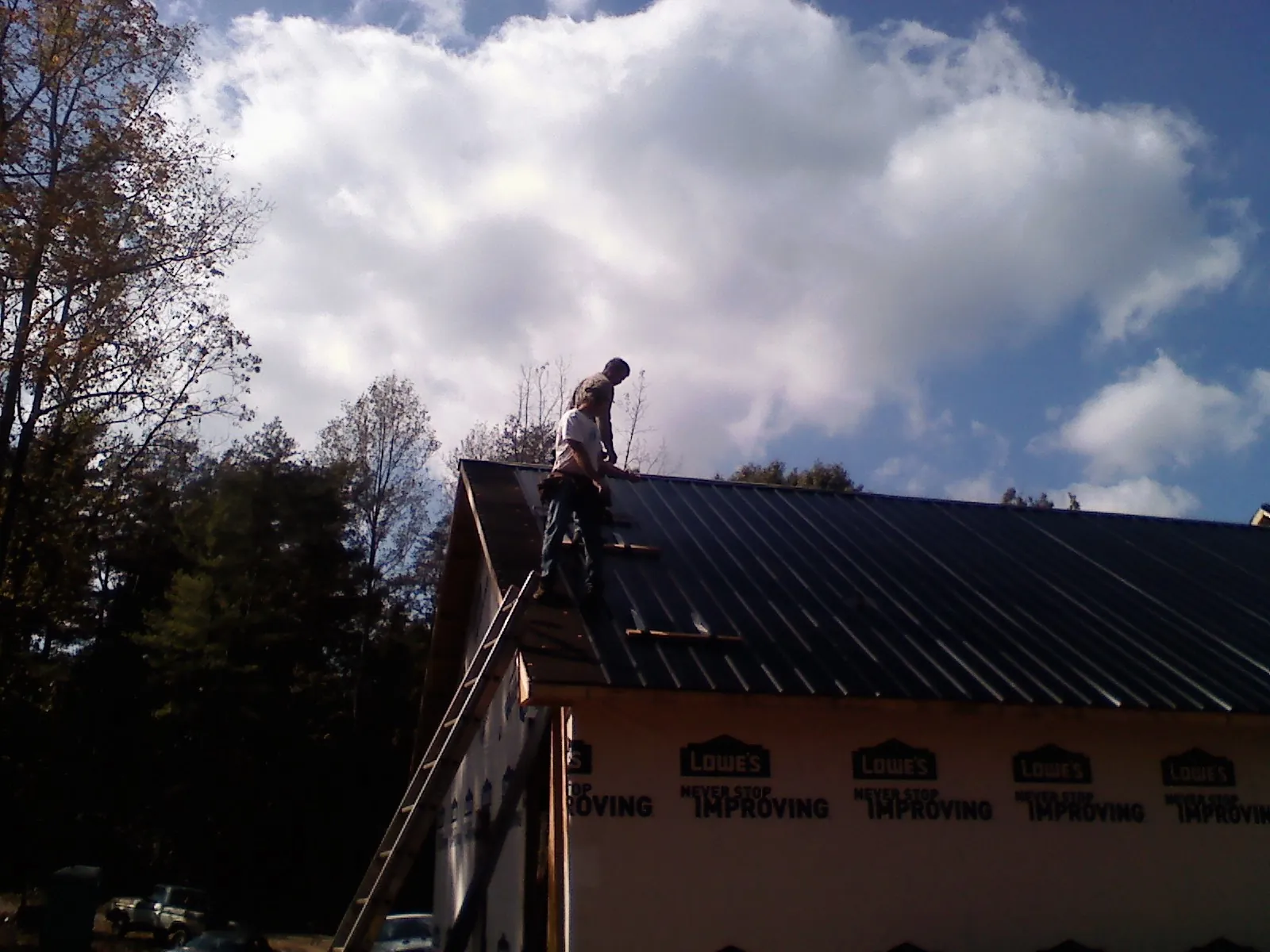 Roofer fastening dark metal panels high against a cloudy sky, from a Roof Inspection job in Crum Lynne