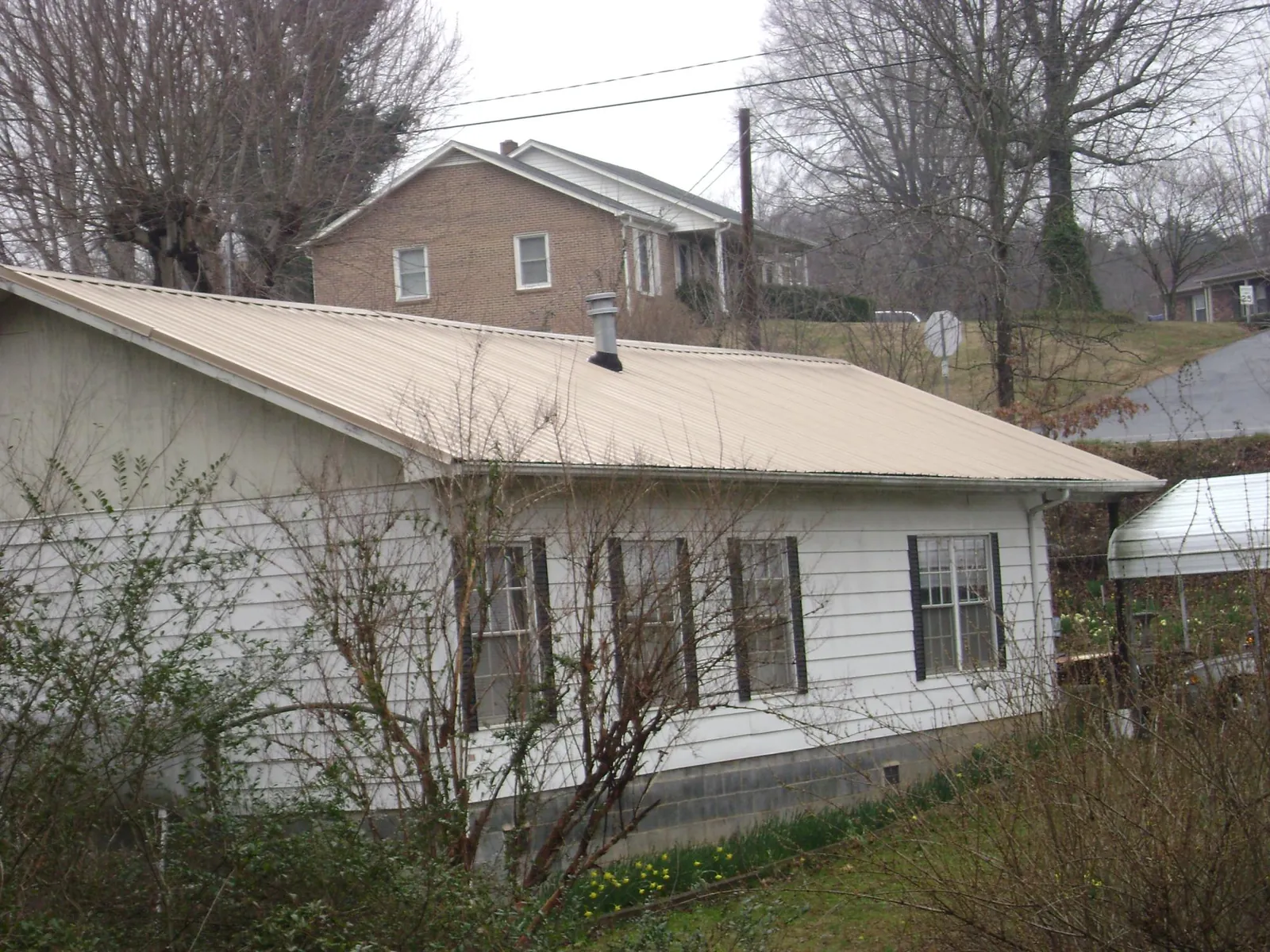 Tan metal roof on a white sided house set into a hillside — Commercial Roofing by Roofing Brothers in Crum Lynne